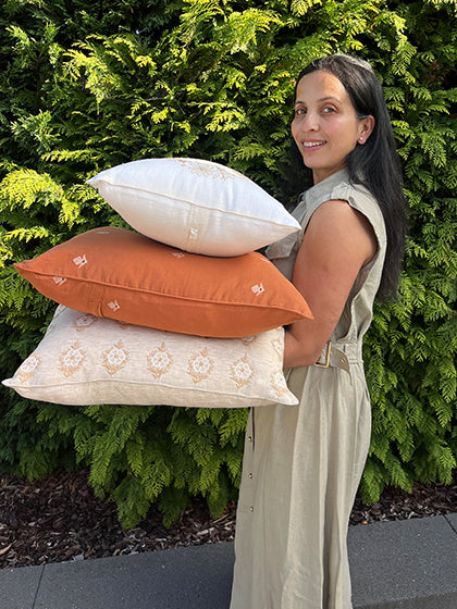 Anshu Gupta, founder of Saaya, holding a stack of pillows against a green bush background