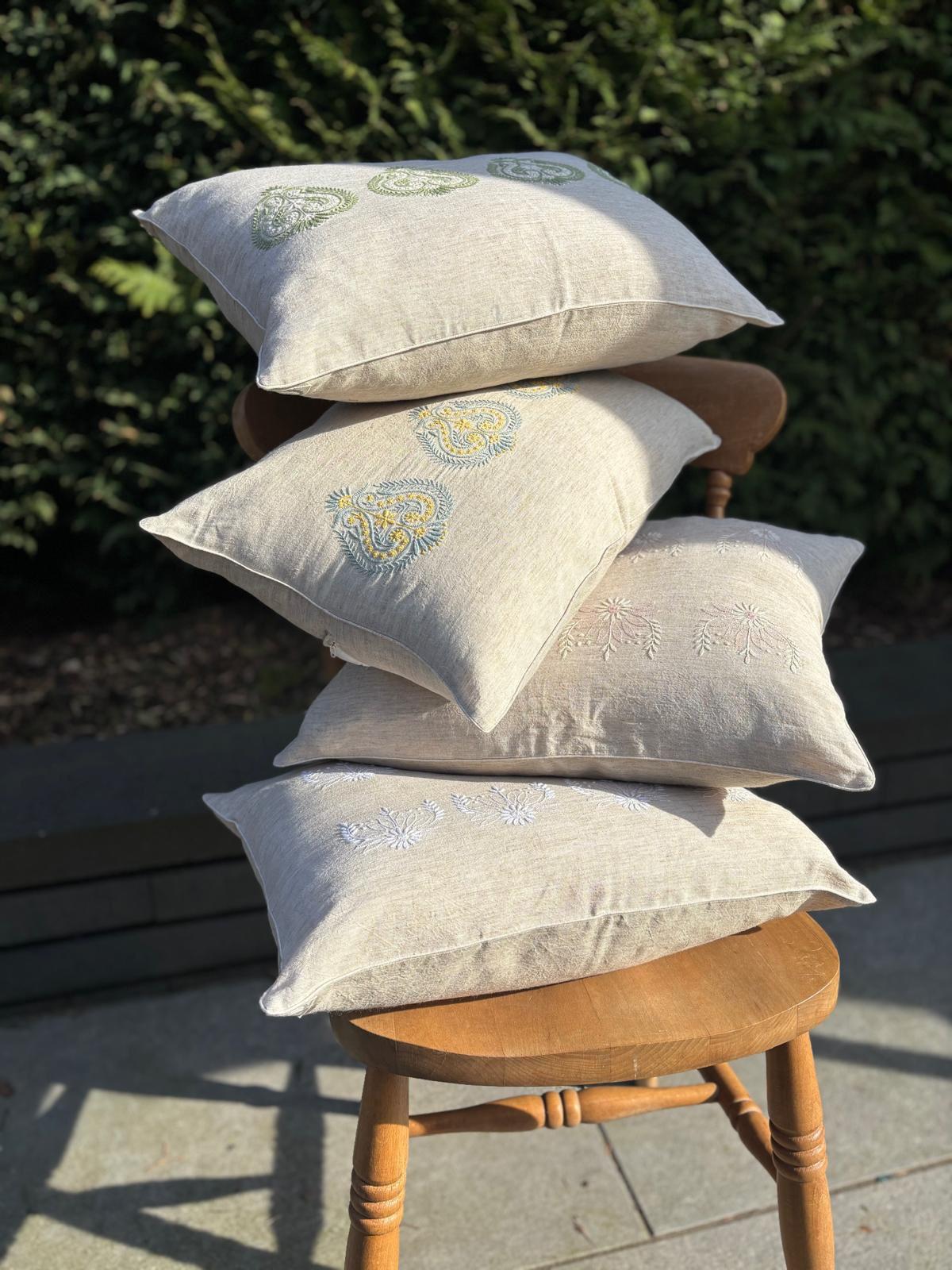 Stack of embroidered chikankari pillows on a wooden stool outdoors.