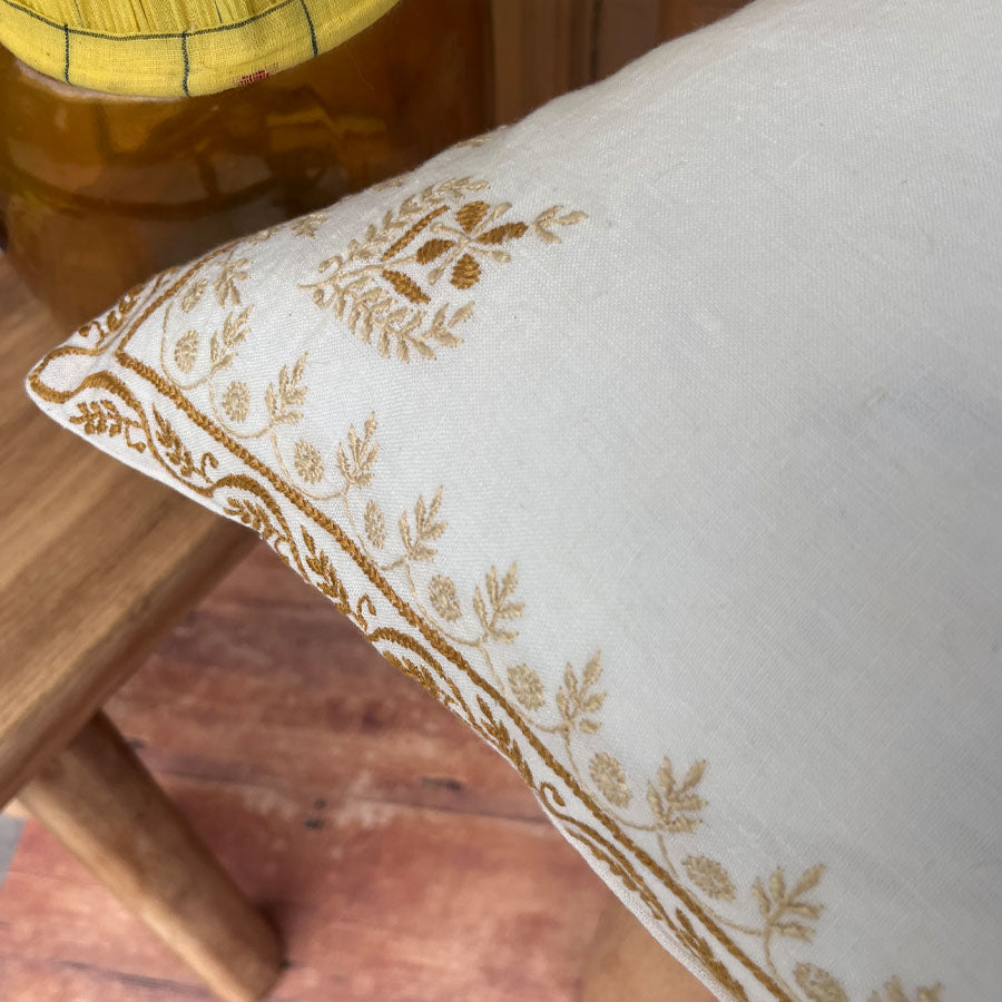 Kinara chikankari cushion cover with gold embroidery on a wooden surface