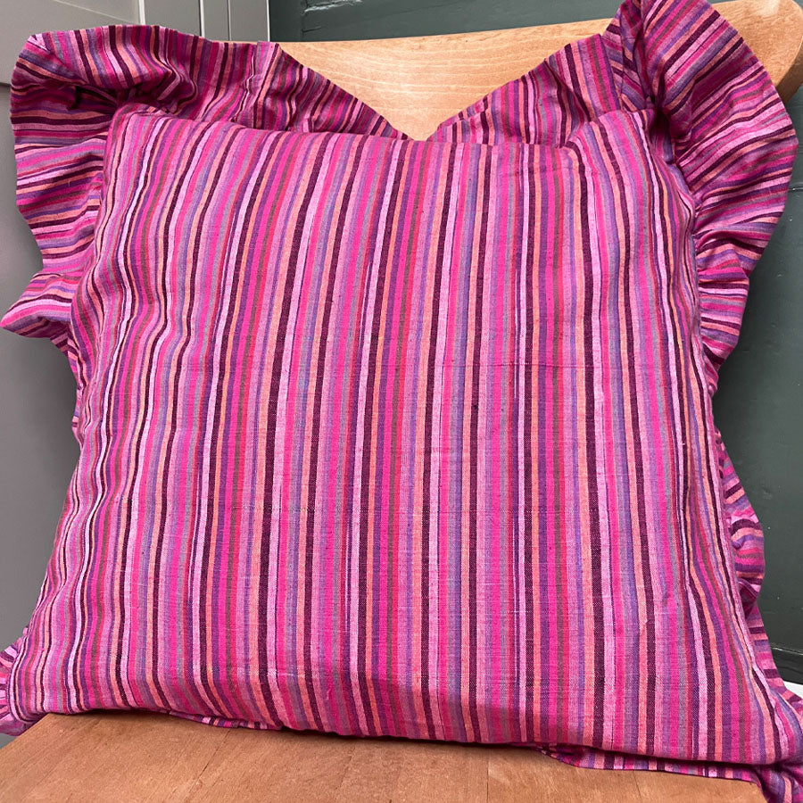 Pink striped pillow cover with ruffled edges on a wooden surface