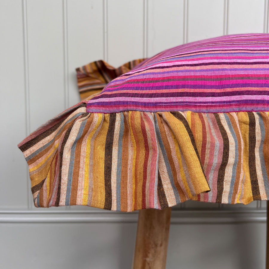 Pink striped pillow cover with yellow striped ruffles on a wooden stool against a white wall