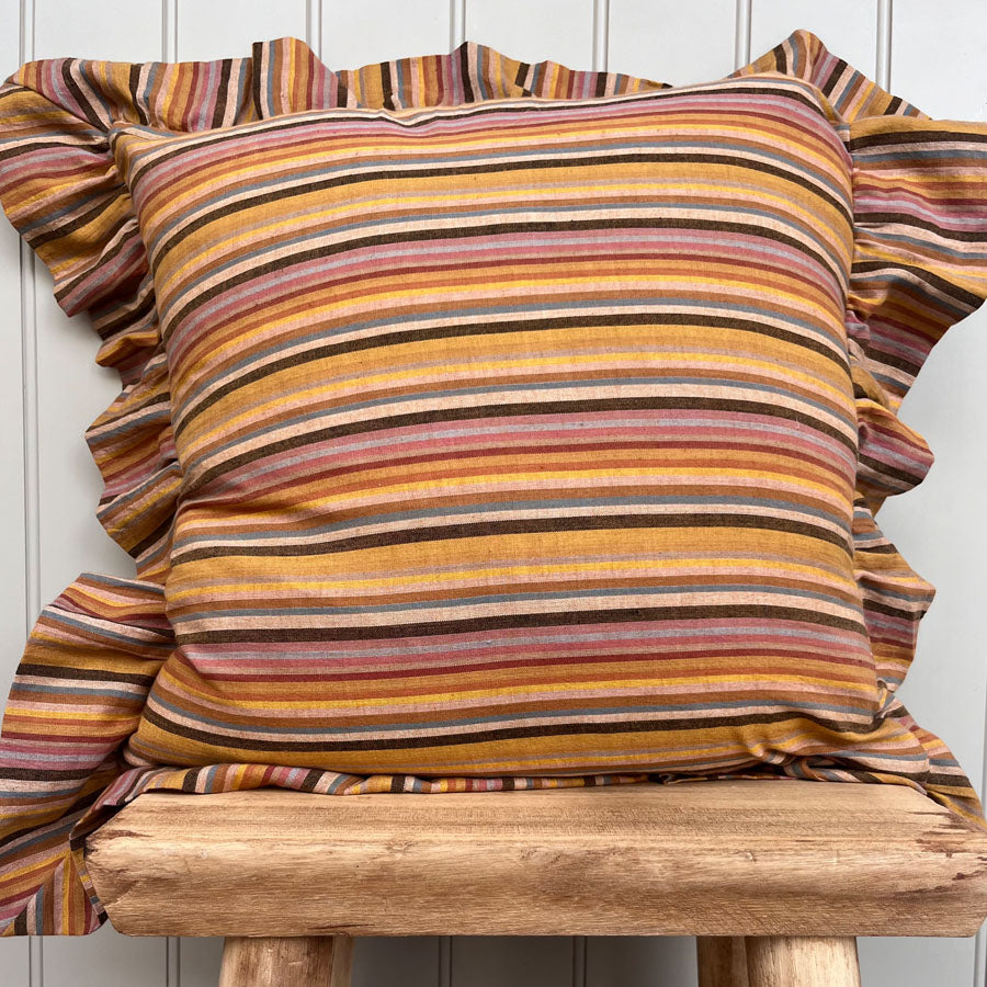 Mustard yellow striped pillow with ruffled edges on a wooden chair against a white wall