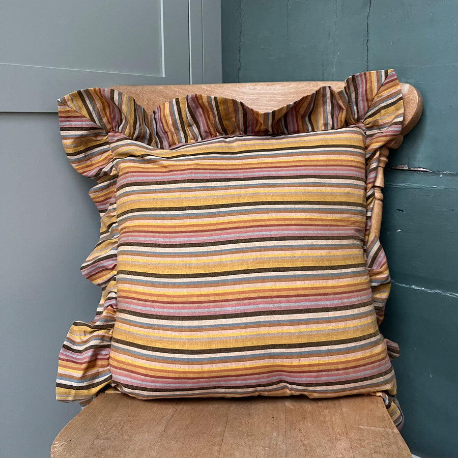 Mustard yellow striped pillow with ruffled edges on a wooden chair against a blue wall.