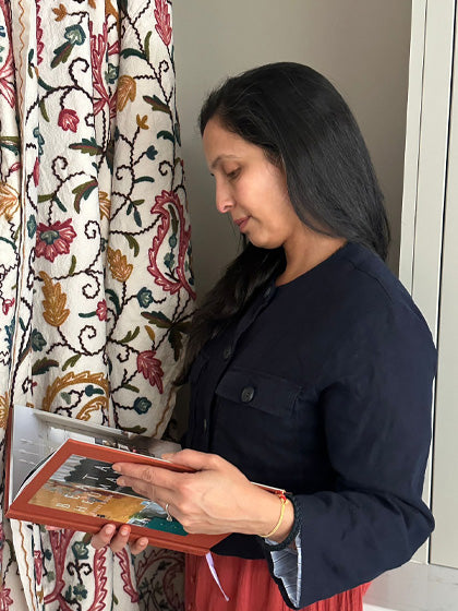 Anshu holding a book in front of a patterned fabric