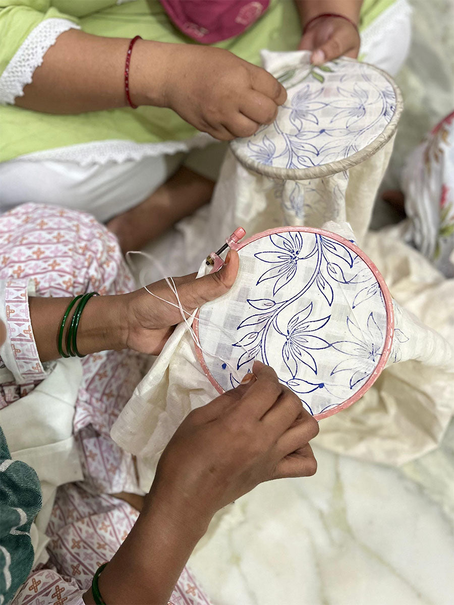 Two people engaged in embroidery work with floral patterns on fabric.