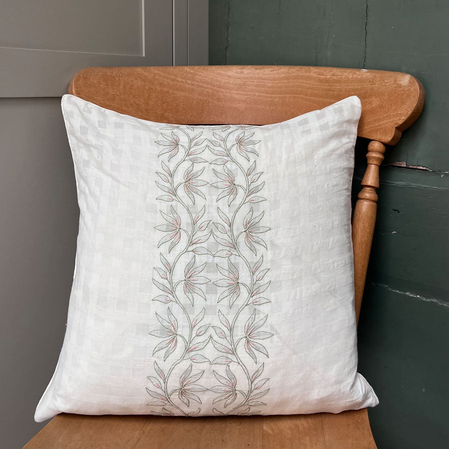 Saaya chikankari cushion cover with lotus bloom embroidery placed on a wooden chair against a grey wall.