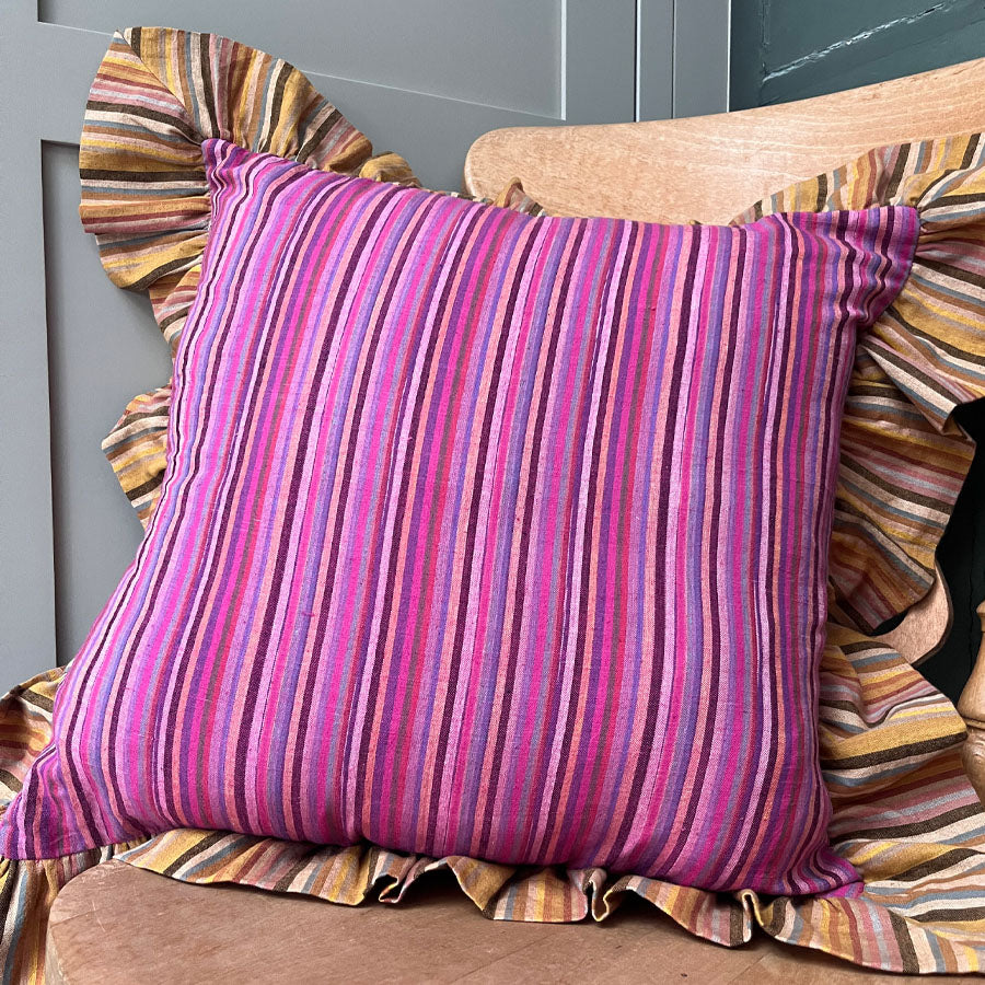 Pink striped pillow cover with yellow striped ruffles on a wooden chair against a grey wall